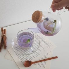 a person is pouring water into a glass teapot with flowers in it and cinnamon sticks on the side