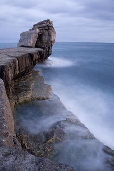 an ocean cliff with water coming out of it and fog in the air around it