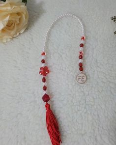 a red tasseled necklace on a white surface next to a flower and a rose