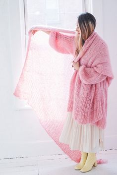 a woman standing in front of a window wearing a pink sweater