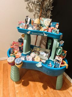 a blue table topped with lots of items on top of a hard wood floor next to a potted plant