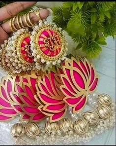 some pink and gold colored jewelry on a white table with green plants in the background