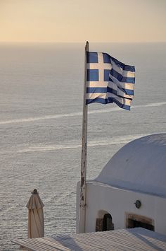 a greek flag flying on top of a building next to the ocean