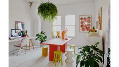 a living room filled with lots of plants next to a white table and two yellow stools