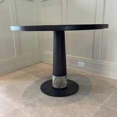 a round table with a black base and grey marble on the top in a room