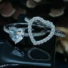 two heart shaped diamond rings on top of a black box with shells in the background