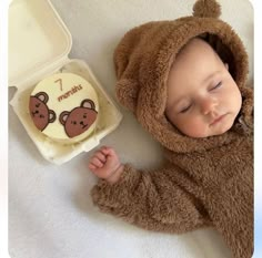 a baby in a bear suit laying next to a container with a cake on it