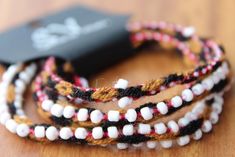 three bracelets with white and red beads on top of a wooden table next to a black box