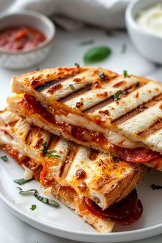 two grilled sandwiches on a white plate with sauces in the bowls behind them