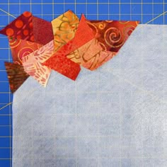 a piece of fabric is being cut into pieces with scissors on the cutting mat next to it