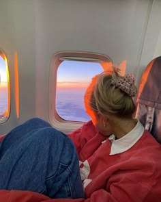 a woman sitting on an airplane seat looking out the window at the sunset and clouds