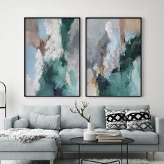 two paintings hang on the wall above a gray couch in a living room with white rugs