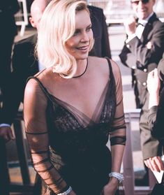 a woman in a sheer black dress standing next to other people and looking off into the distance