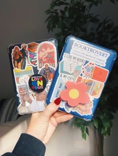 a person holding up two book covers with stickers on them and a flower in the middle