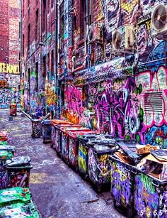 an alleyway with graffiti all over the walls and trash cans on the sidewalk next to it