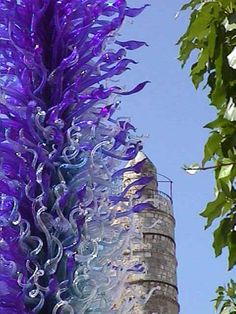 a tall purple flower sitting next to a tree