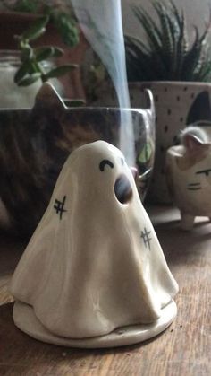 a white ghost figurine sitting on top of a wooden table next to potted plants