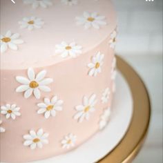 a pink and white cake with daisies on the top is sitting on a gold stand