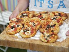 several small pizzas sitting on top of a wooden cutting board next to a person