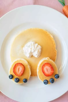 a white plate topped with pancakes covered in whipped cream and blueberries next to a carrot