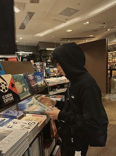 a person in a black hoodie is looking at some books on a book shelf