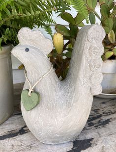 a ceramic bird with a tag on it's neck sitting next to potted plants