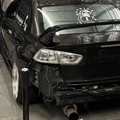 a car that is being worked on in a garage, with the hood up and front bumper removed