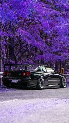 the car is parked on the side of the road with purple trees in the background