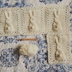 a crocheted blanket and two knitting needles on a tablecloth with blue floral designs