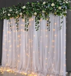 the curtain is decorated with white flowers and greenery, while lights shine down on it