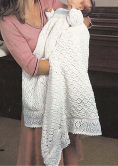 a woman holding a baby wrapped in a white crochet blanket next to a piano