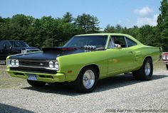 a green and black car parked in a parking lot next to other cars with trees in the background