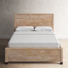 a wooden bed frame with white pillows and sheets on it, in a light colored room