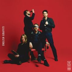 three men sitting on a red chair in front of a red background with the caption's name