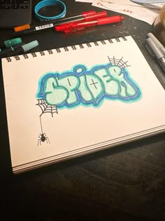 a notebook with the word spider written in blue on it next to markers and pens