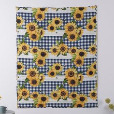 a blue and white checkered table cloth with sunflowers on it is hanging from the wall