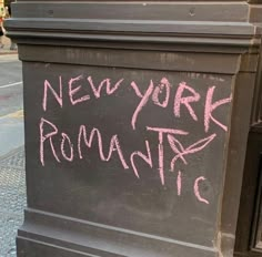 a chalkboard with the words new york romantic written in pink ink on it next to a sidewalk