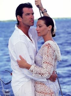 a man and woman on a boat in the ocean hugging each other while holding an umbrella