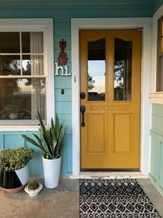 a yellow front door with two potted plants on the side and an entrance mat