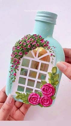 a hand holding a bottle with flowers painted on the front and side, which has a window in it