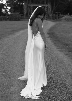 a woman in a wedding dress is standing on the road with her back to the camera