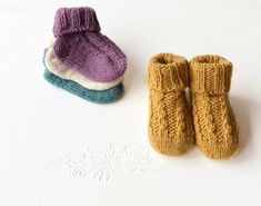 three knitted baby booties sitting next to each other on a white surface with snowflakes