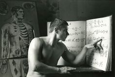 a shirtless man writing on an open book in front of skeleton drawings and human figures