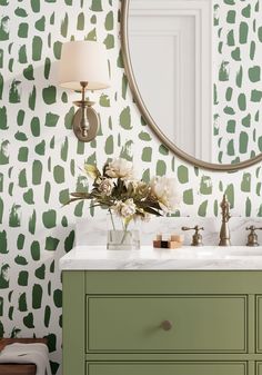 a bathroom with green and white wallpaper, a round mirror and two sinks in front of it