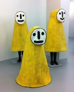 three yellow figures with faces painted on them are standing in front of a white wall