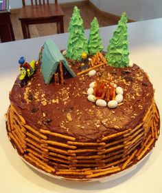 a chocolate cake decorated with trees, rocks and campfires on a white table