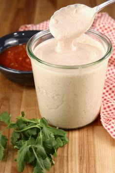 a spoon full of dressing sitting on top of a wooden table next to a bowl of sauce