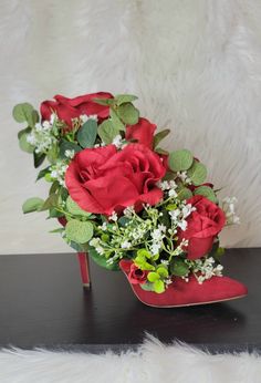 a bouquet of red roses and baby's breath sits on top of a high heeled shoe