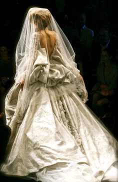 a woman in a white wedding gown and veil walking down the runway at a fashion show