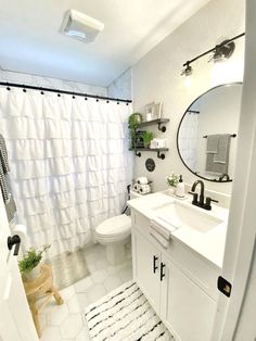 a white bathroom with a shower curtain and rug on the floor next to the sink